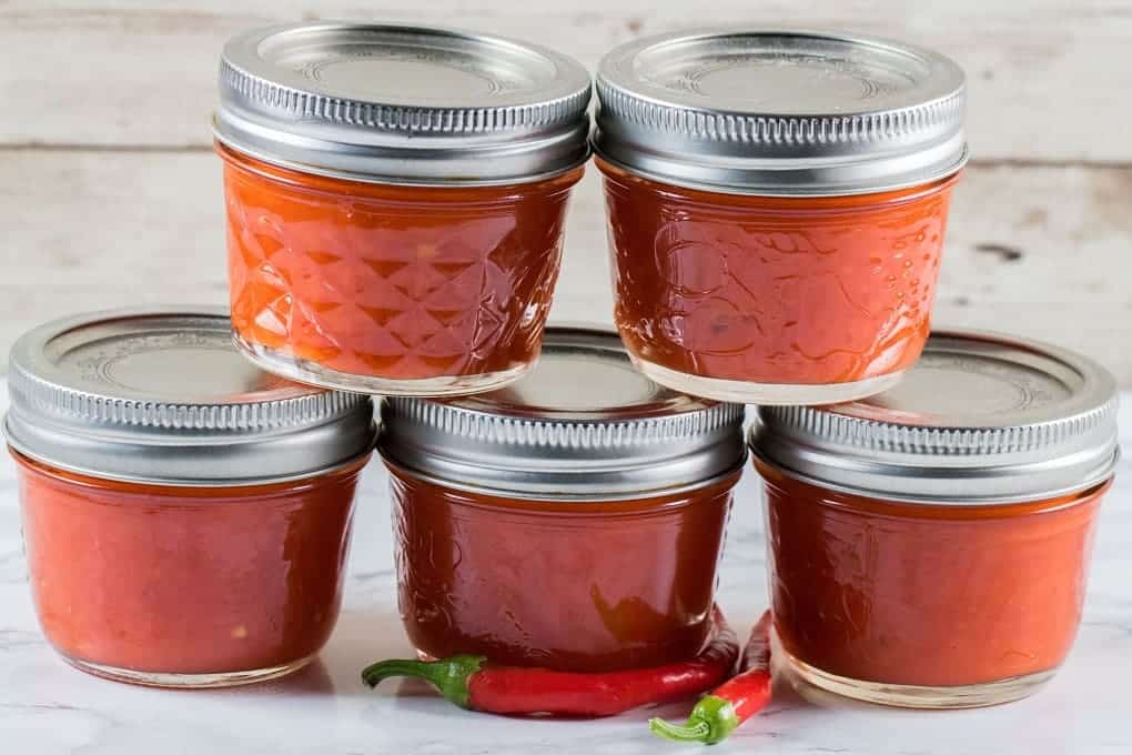 homemade pepper sauce in jars placed on a smooth surface with chillies