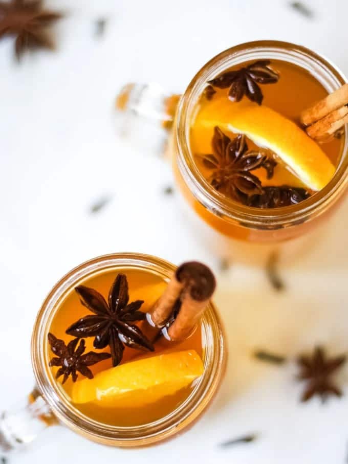 jars filled with mulled cider along with cinnamon sticks star anise and some apple and oranges