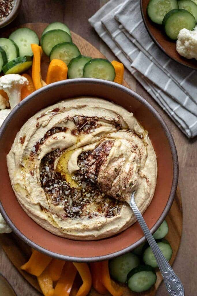 zaatar hummus in a bowl with a ladle some fresh veggies on side