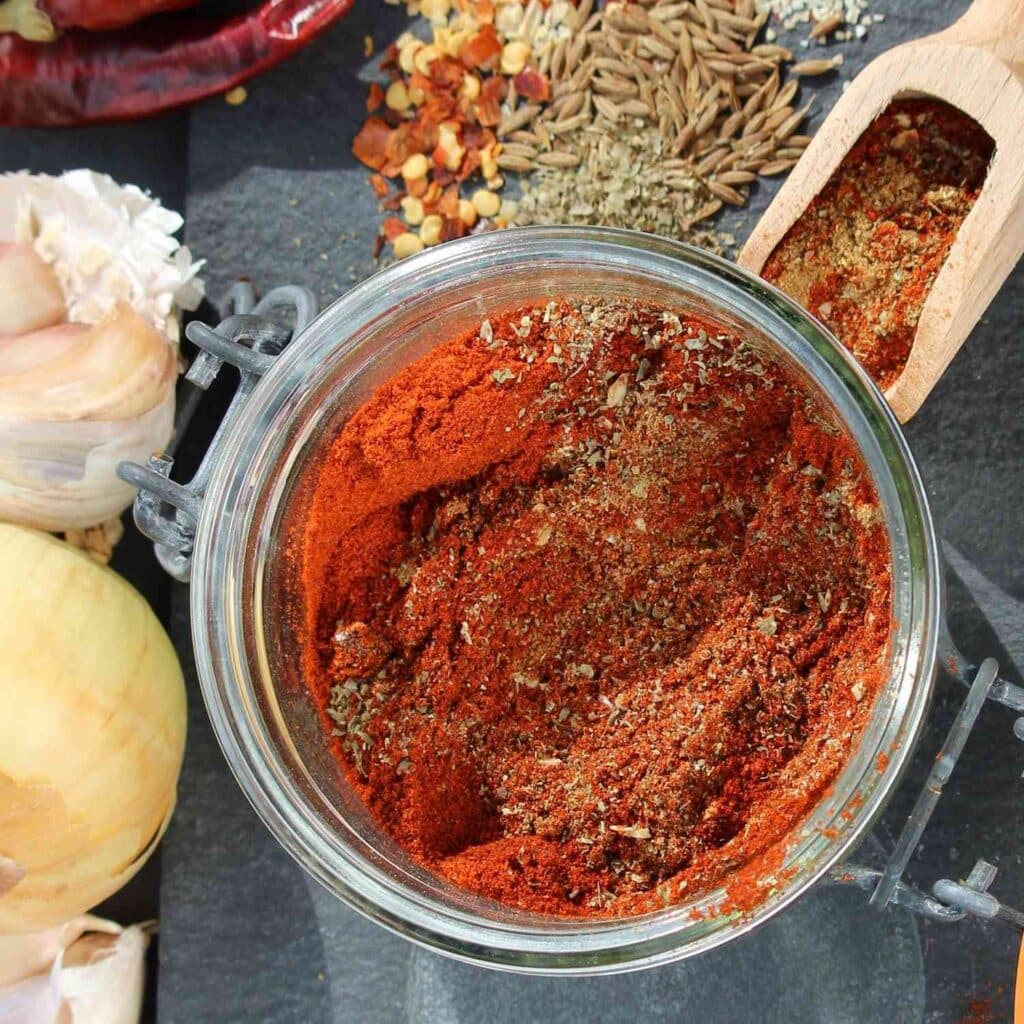 Homemade Chili Powder in a jar with garlic and cumin seeds in the background