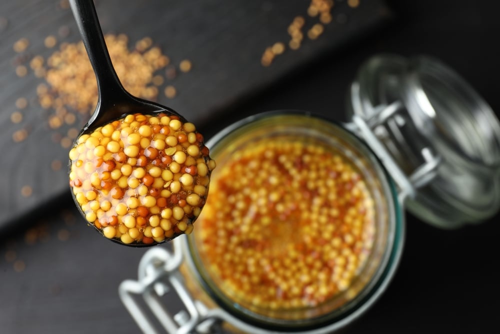 Spoon With Whole Grain Mustard Over Jar On Table Closeup