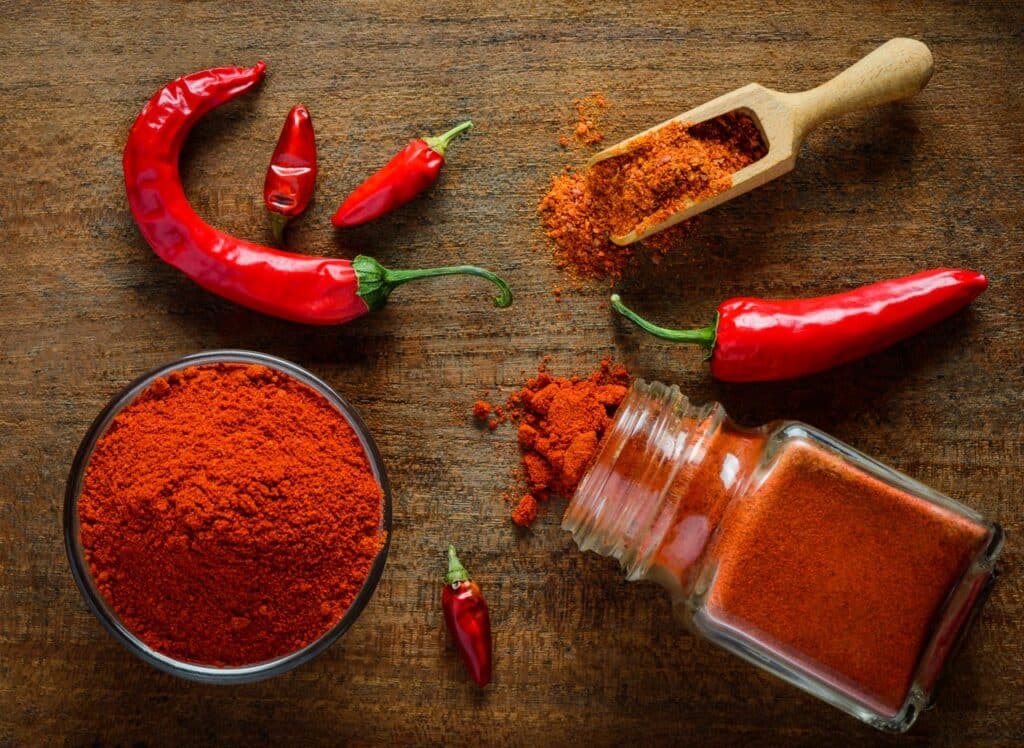 a bowl and a jar of paprika along with whole red peppers placed on a wooden surface