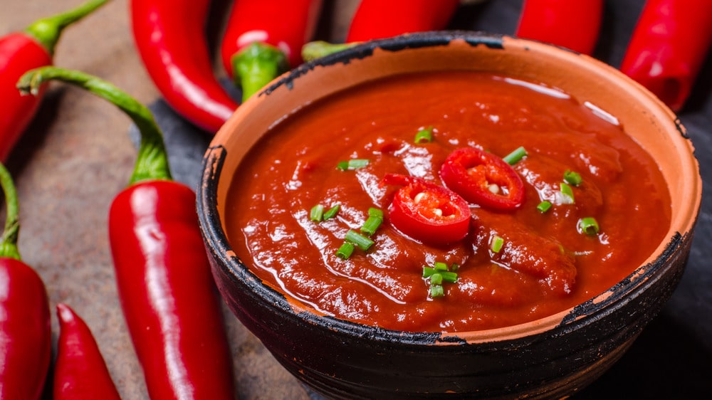 a bowl full of hot sauce garnished with red peppers and whole red peppers in background