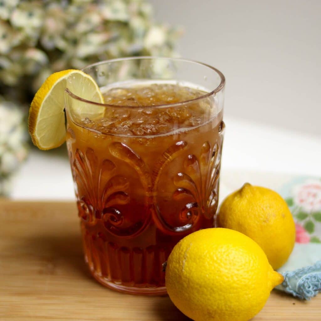 a glass of mace and nutmeg spiced tea garnished with a lemon wedge and a whole lemon placed nearby