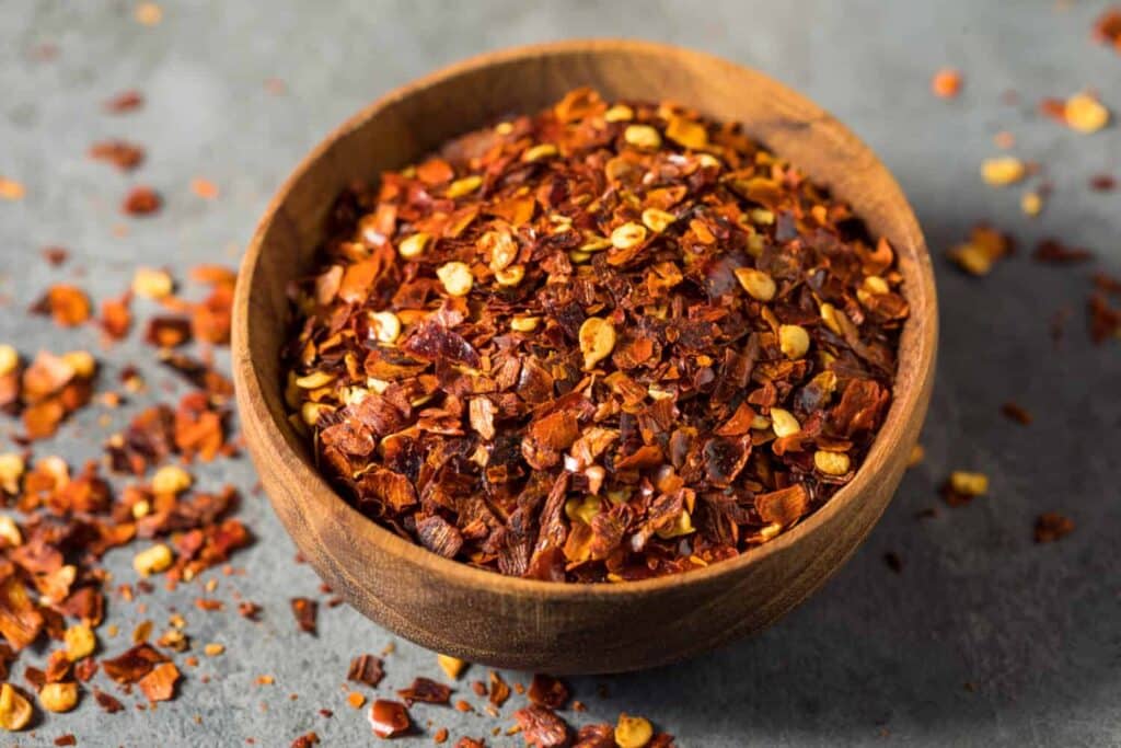 a wooden bowl full of red pepper flakes along with sprinkled flakes on the surface