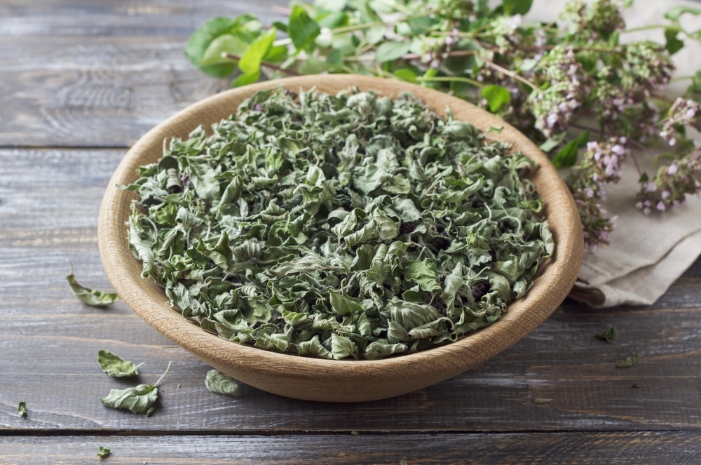 Dried oregano leaves in a wooden bowl on a wooden table with fresh oregano, top view, close up