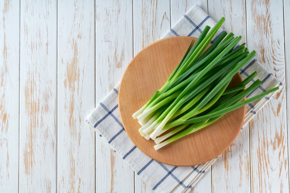 Fresh spring onions or scallions on a cutting board on white wooden table