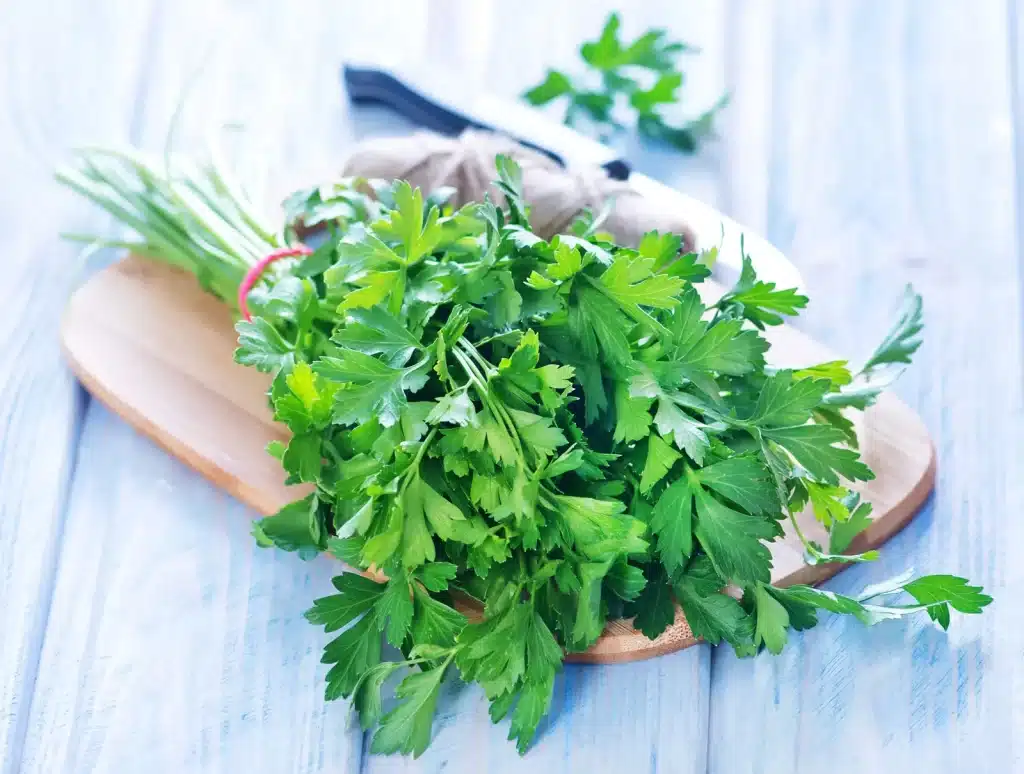 parsley placed on a wooden plate wiht blurred view of knife