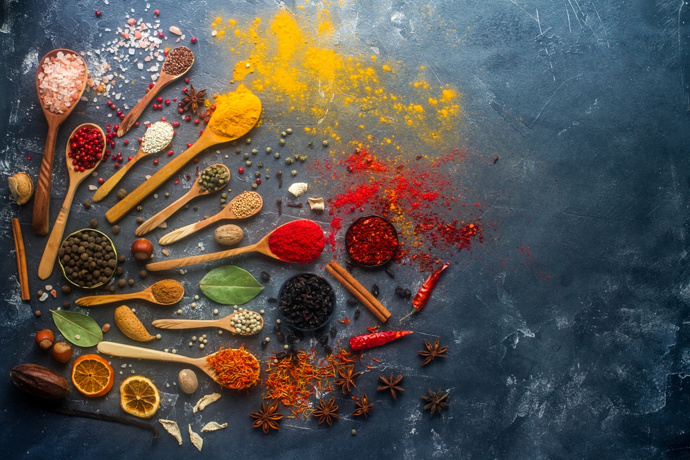 a vairiety of seasonings in wooden spoons placed on a black surface