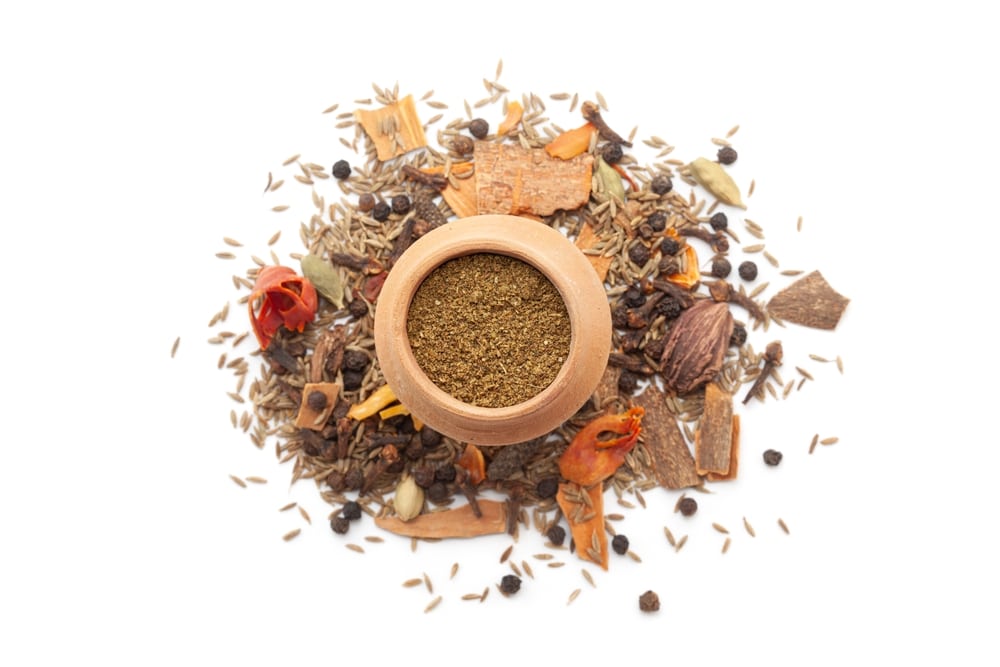 A mud pot filled with organic warming spices or whole Garam Masala powder, placed on a heap of whole spices